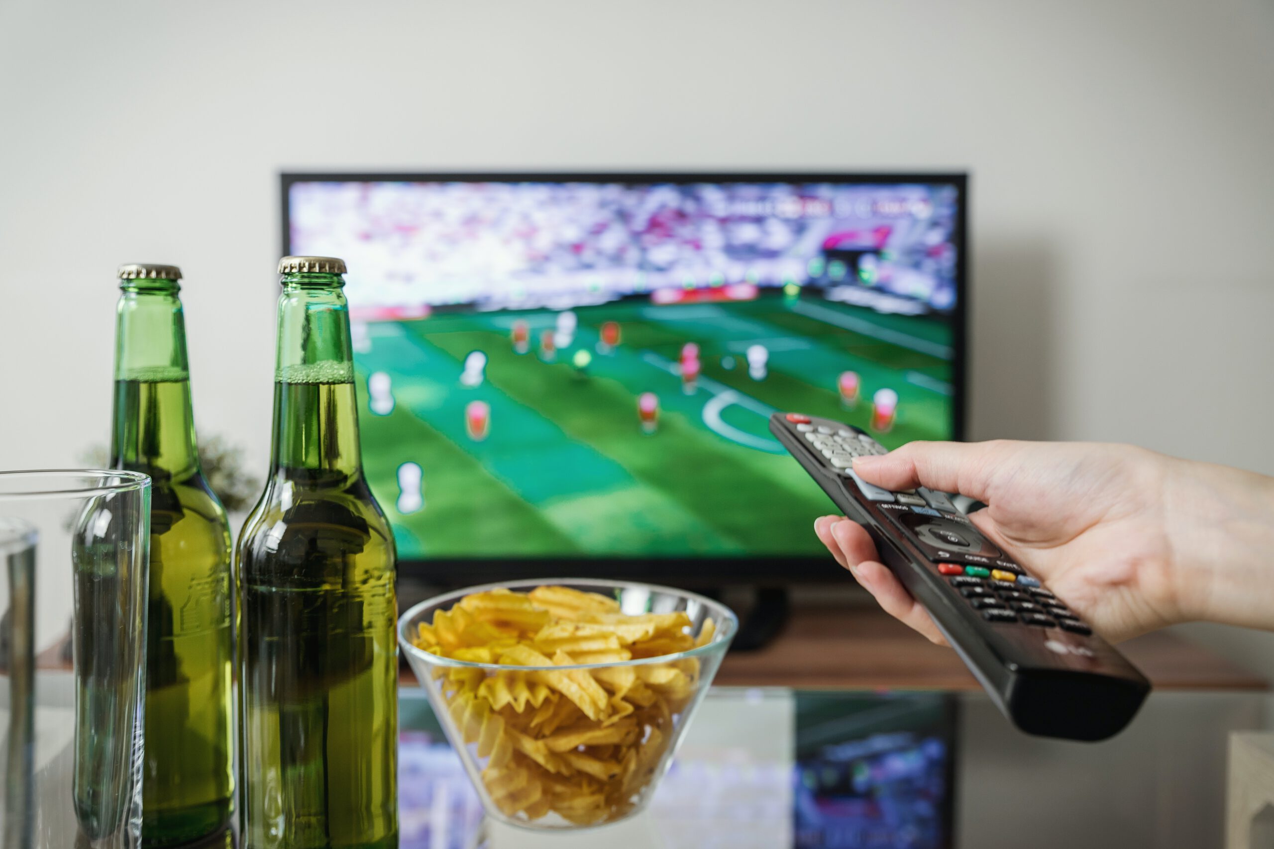 Mężczyzna z pilotem w ręce i piwem oraz chipsami na stoliku oglądający mecz w telewizji