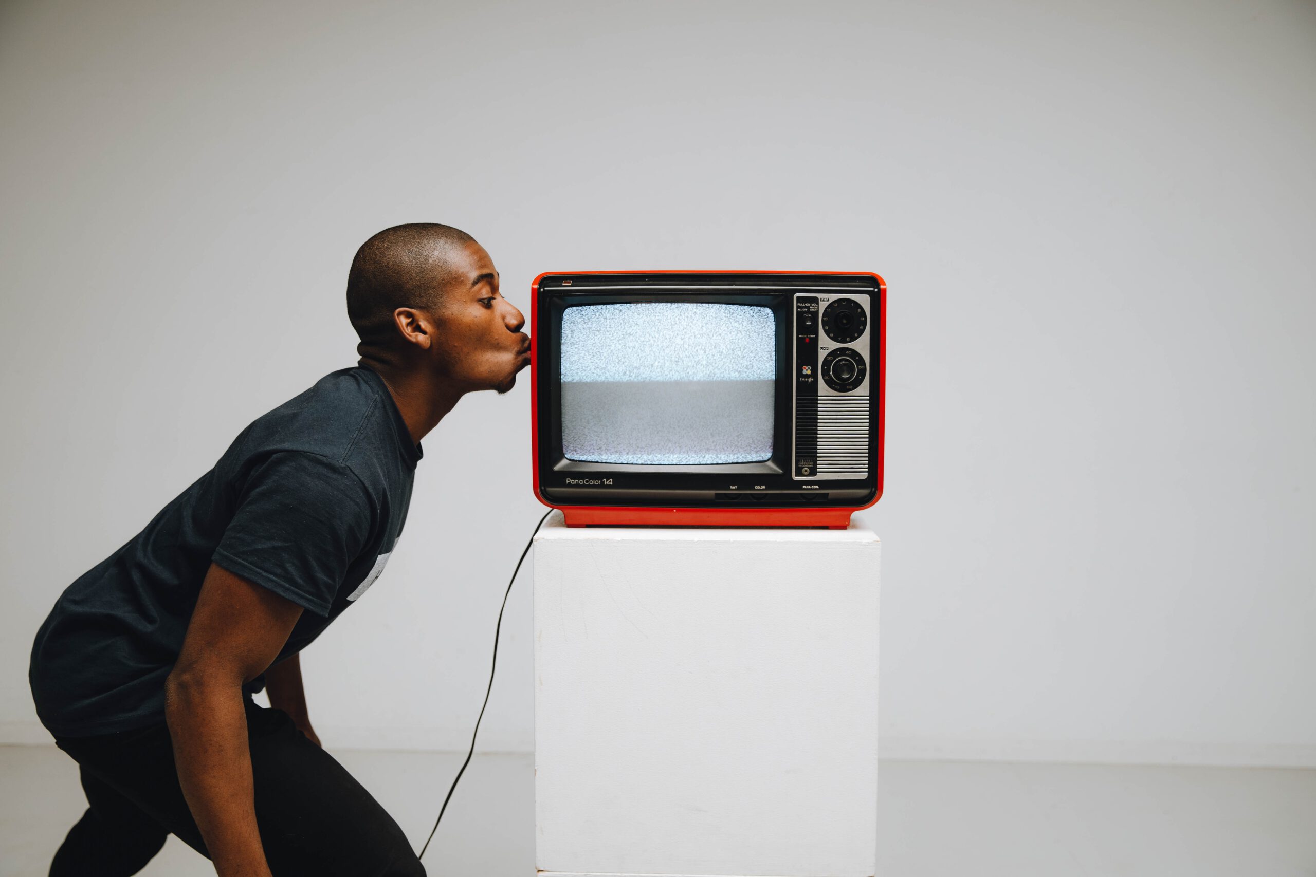 Młody mężczyzna całujący czerwony telewizor stojący na białym tle